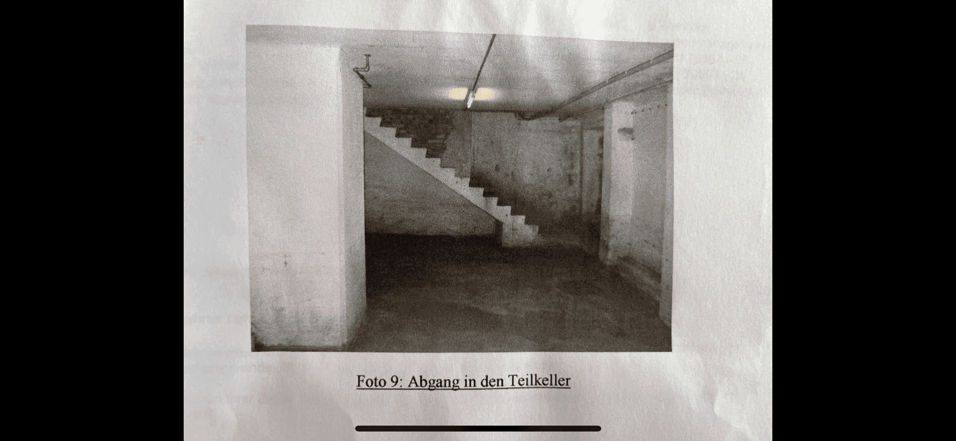 Foto eines Treppenabgangs in einen Teilkeller mit rauen Wänden, Betonboden und einfacher Beleuchtung.