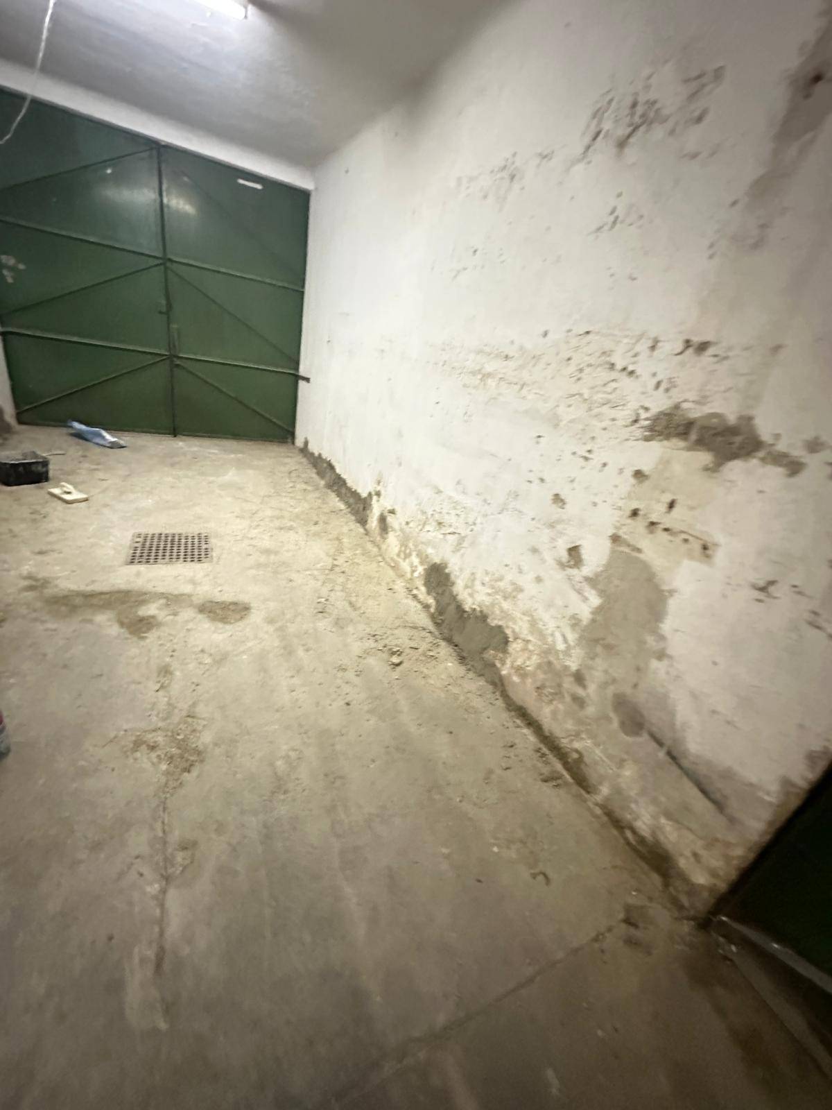 Innenansicht einer Garage mit grünem Tor, Betonboden und abblätternder Farbe an den Wänden, deutliche Abnutzung sichtbar.