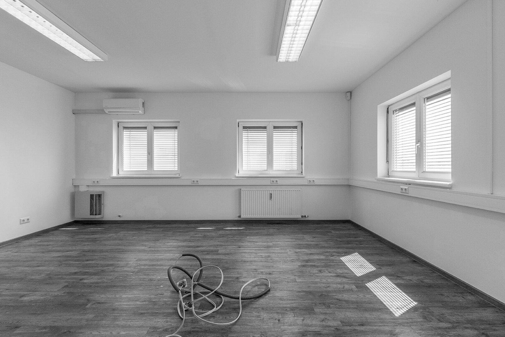 Büroraum mit Laminatboden, Jalousien an den Fenstern und einer Klimaanlage an der Wand.