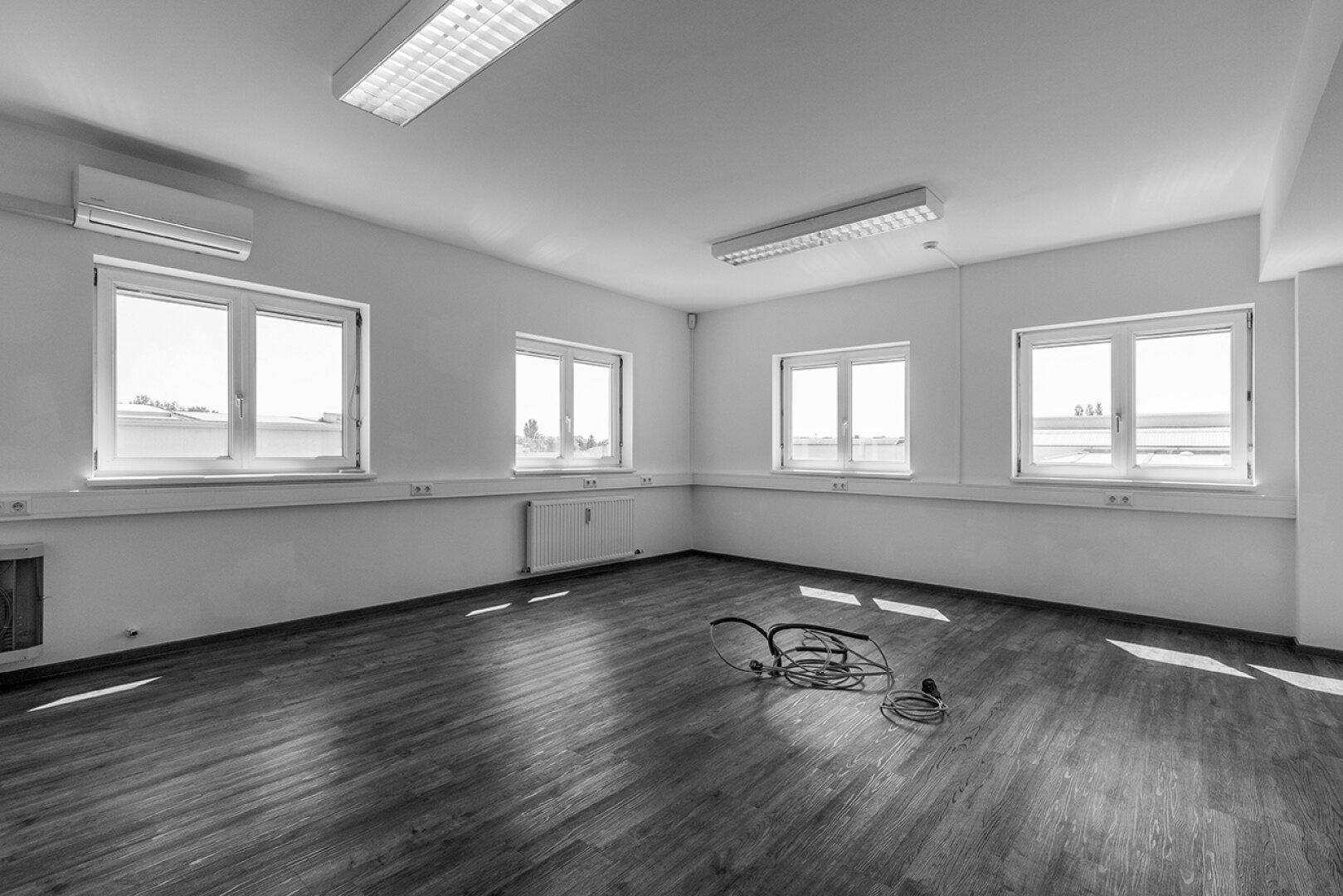 Leeres Büro mit Laminatboden, Klimaanlage und mehreren Fenstern, die viel Licht hereinlassen.