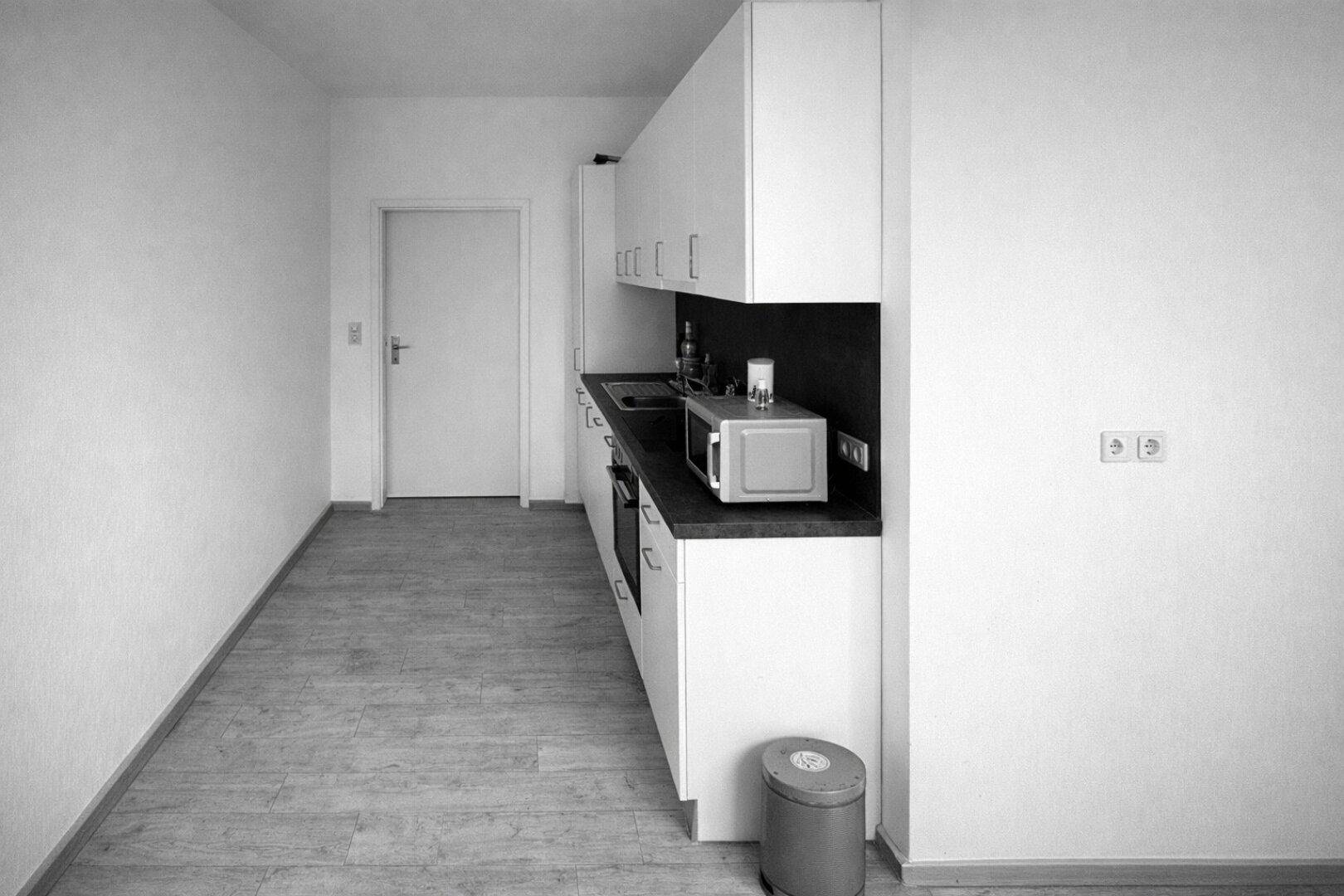 Kleine Küchenzeile mit weißen Schränken, dunkler Arbeitsplatte und integrierten Geräten.