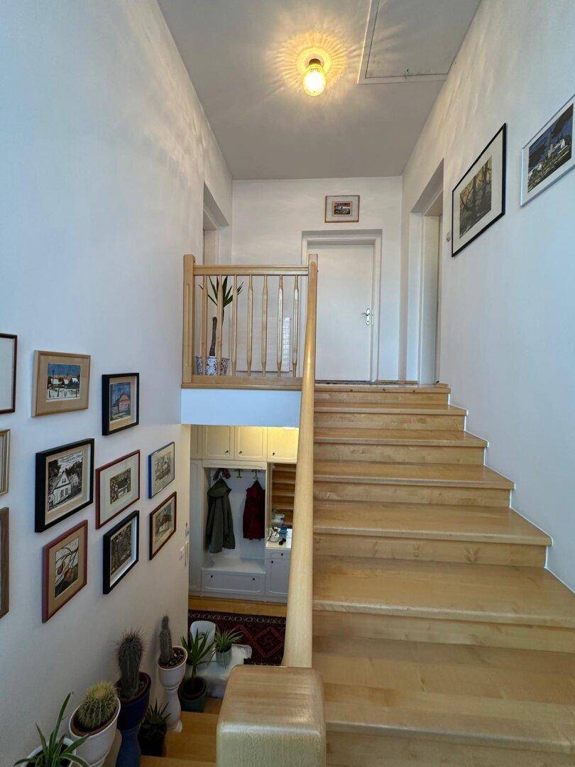 Helles Treppenhaus mit Holzgeländer und integrierter Garderobe im unteren Bereich.