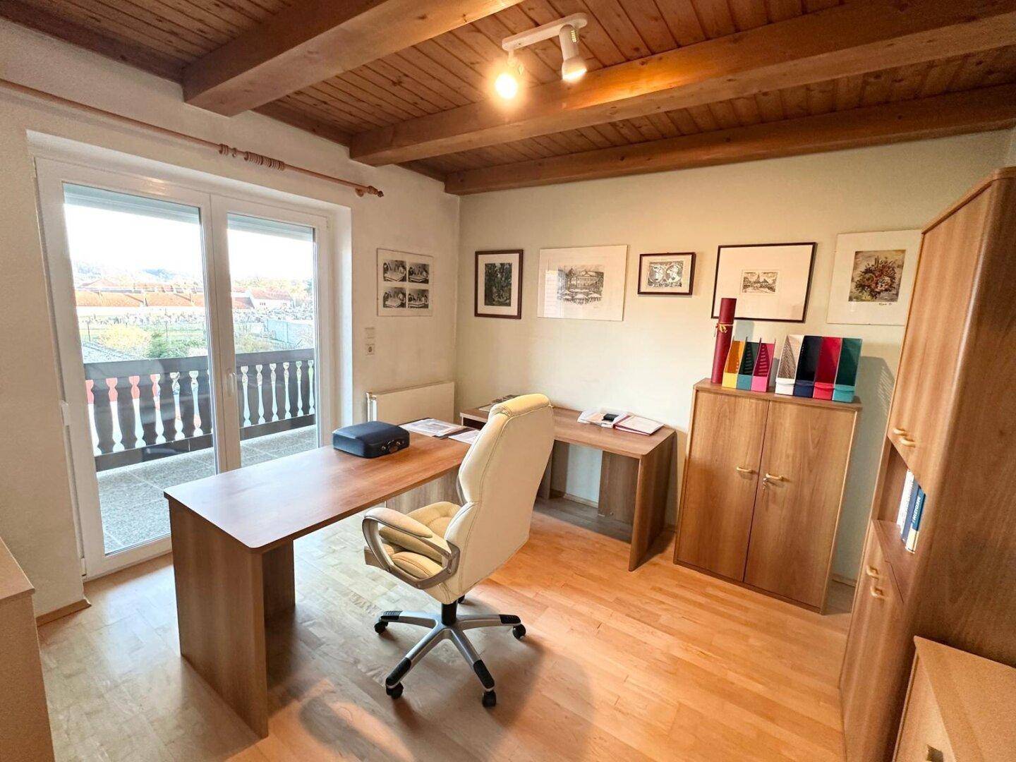 Arbeitszimmer mit Holzmöbeln, sichtbaren Deckenbalken und Zugang zum Balkon.
