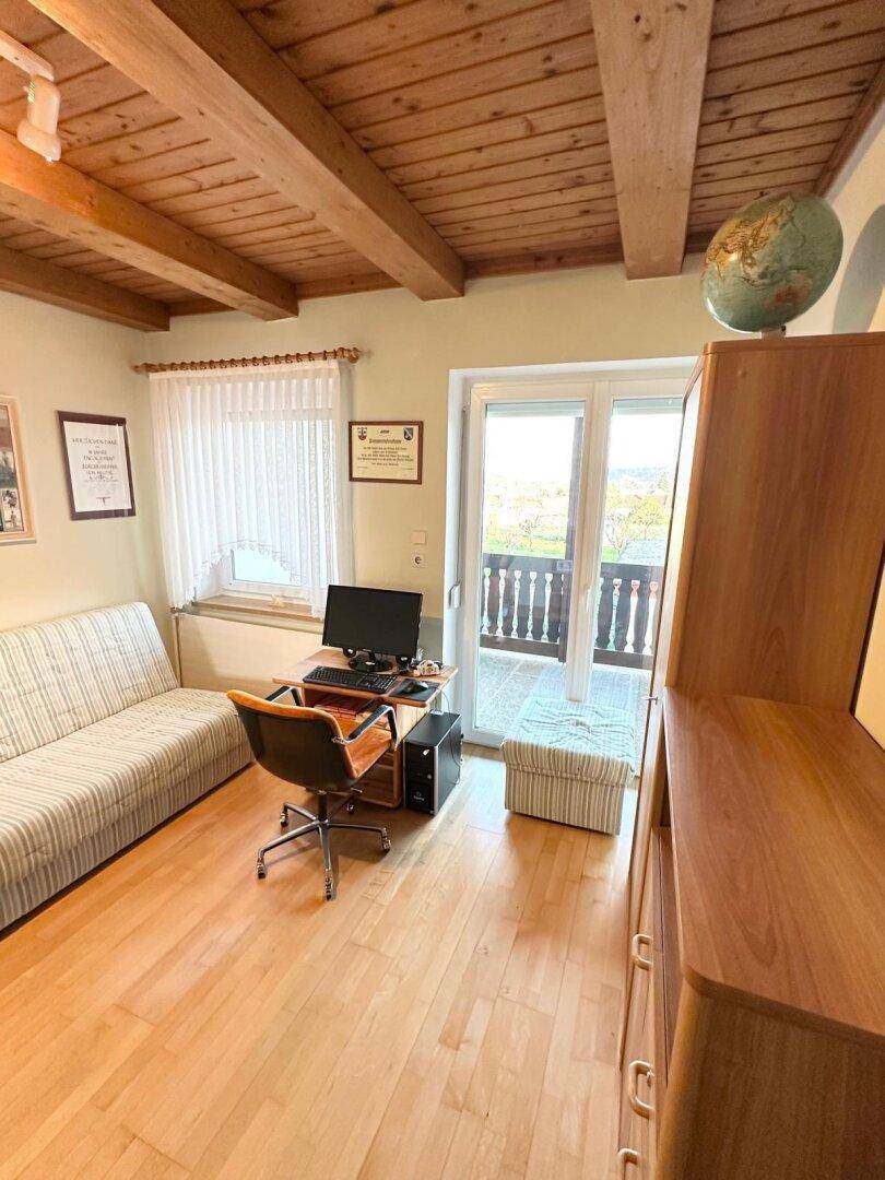 Helles Arbeits- oder Gästezimmer mit Sofa, Schreibtisch und Balkonzugang.