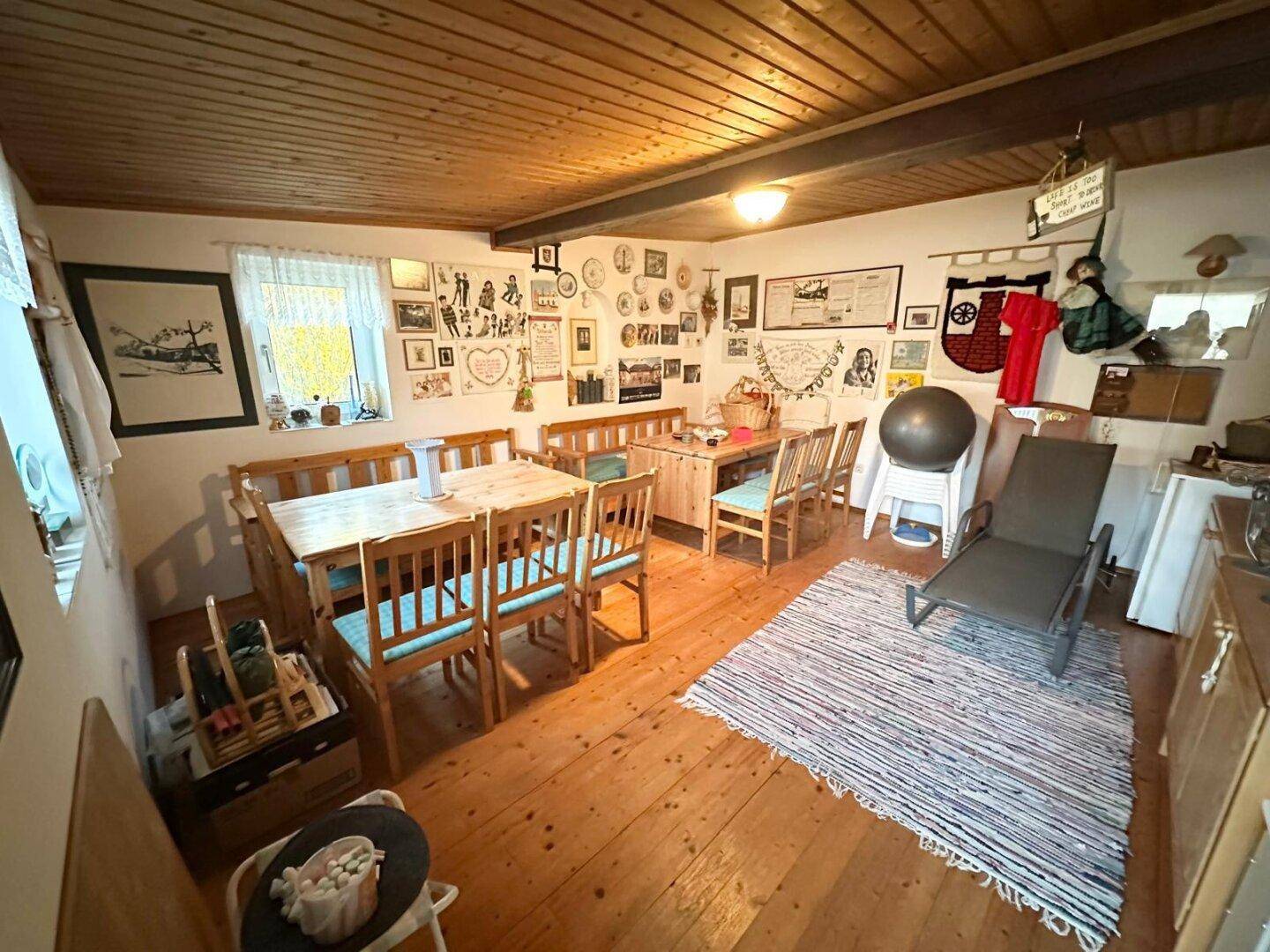 Rustikaler Wohn-Essbereich mit Holztischen, Bänken und sichtbarer Holzdecke.