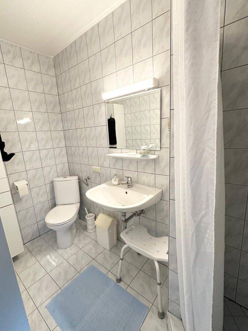 Gefliestes Badezimmer mit Toilette, Waschbecken und einer Duschkabine mit Vorhang.