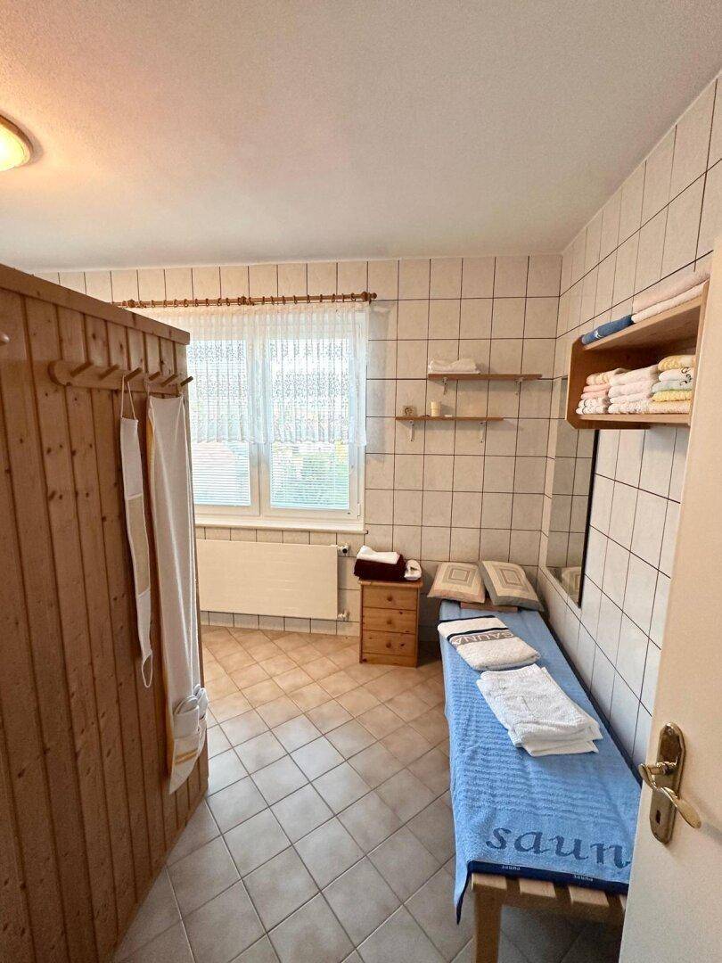 Entspannungsbereich mit einer Saunakabine, gefliestem Boden und einer Liege.