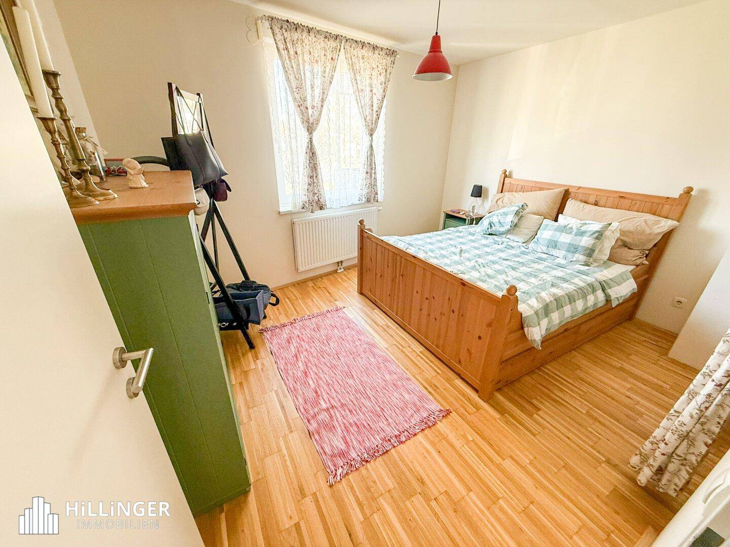 Gemütliches Schlafzimmer mit Holzbett, Kommode und Fenster, das viel Tageslicht hereinlässt.