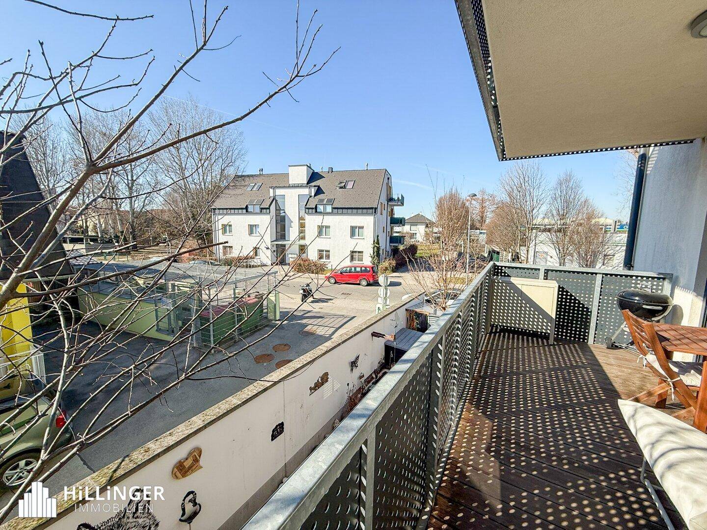 Großer Balkon mit Holzboden, Grill und Blick auf die umliegenden Häuser und die Straße.