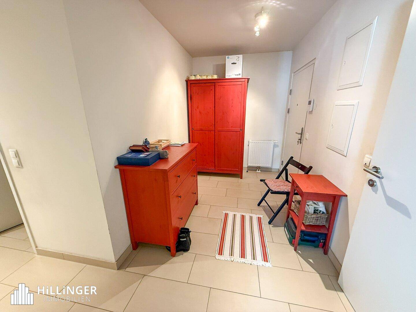 Eingangsbereich mit roten Möbeln, Fliesenboden und Zugang zur Wohnungstür.