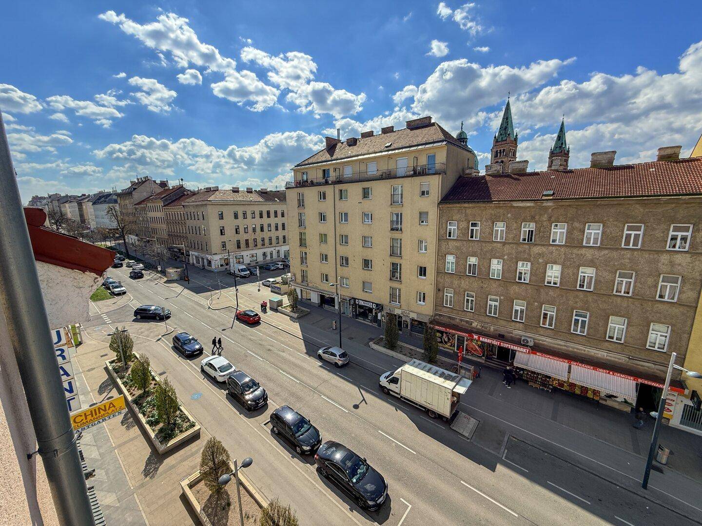 Weitläufiger Blick über eine Stadtstraße mit Gebäuden und Kirchtürmen im Hintergrund.