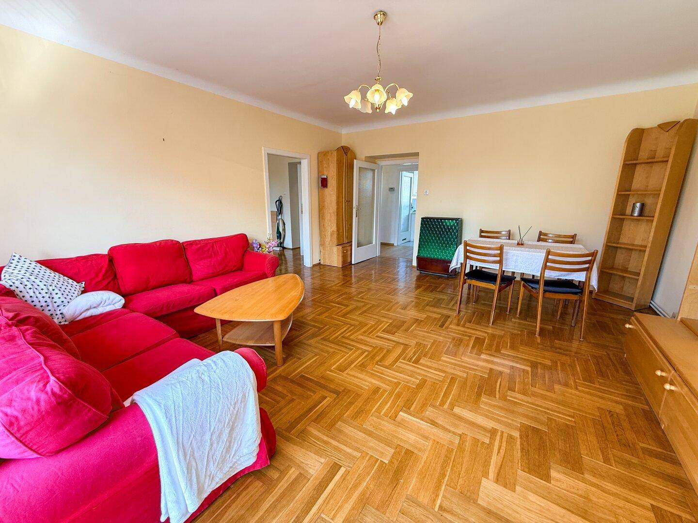 Heller Wohn- und Essbereich mit Parkettboden, rotem Sofa und Blick auf weitere Räume.