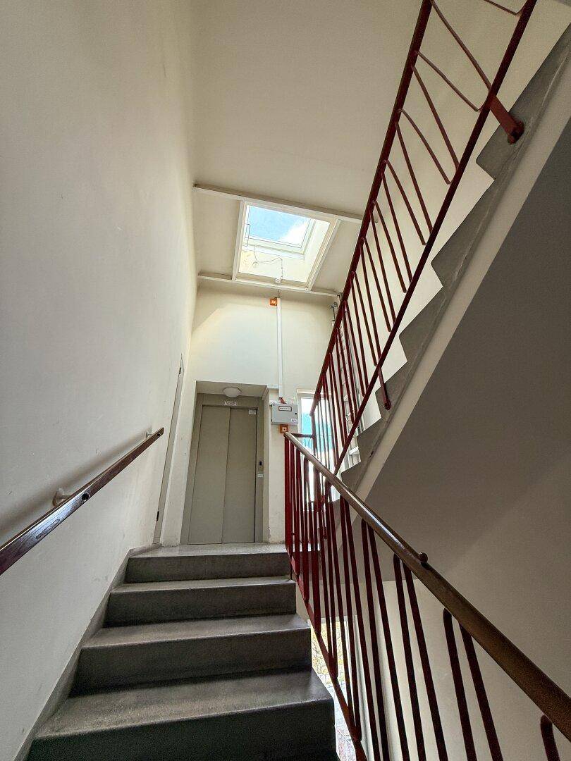 Treppenhaus mit Geländer, Aufzug und einem Oberlicht, das natürliches Licht spendet.