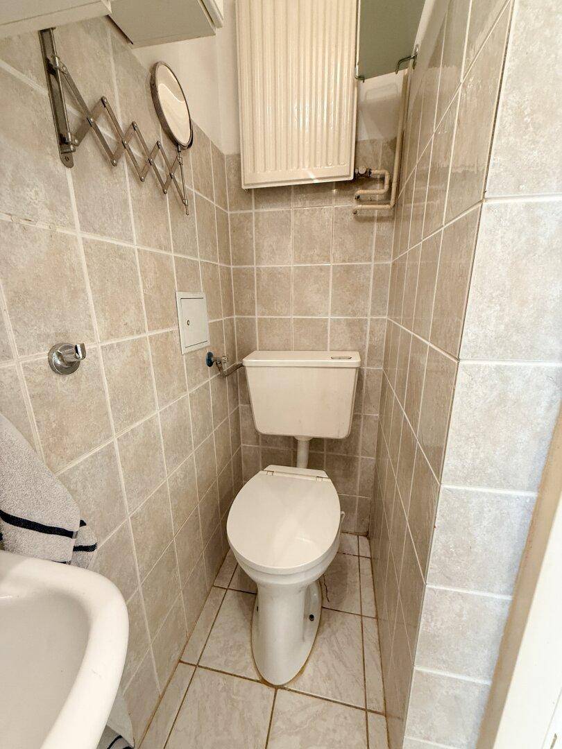 Kleine Toilette mit WC, Waschbecken und hellen Fliesen an Wänden und Boden.