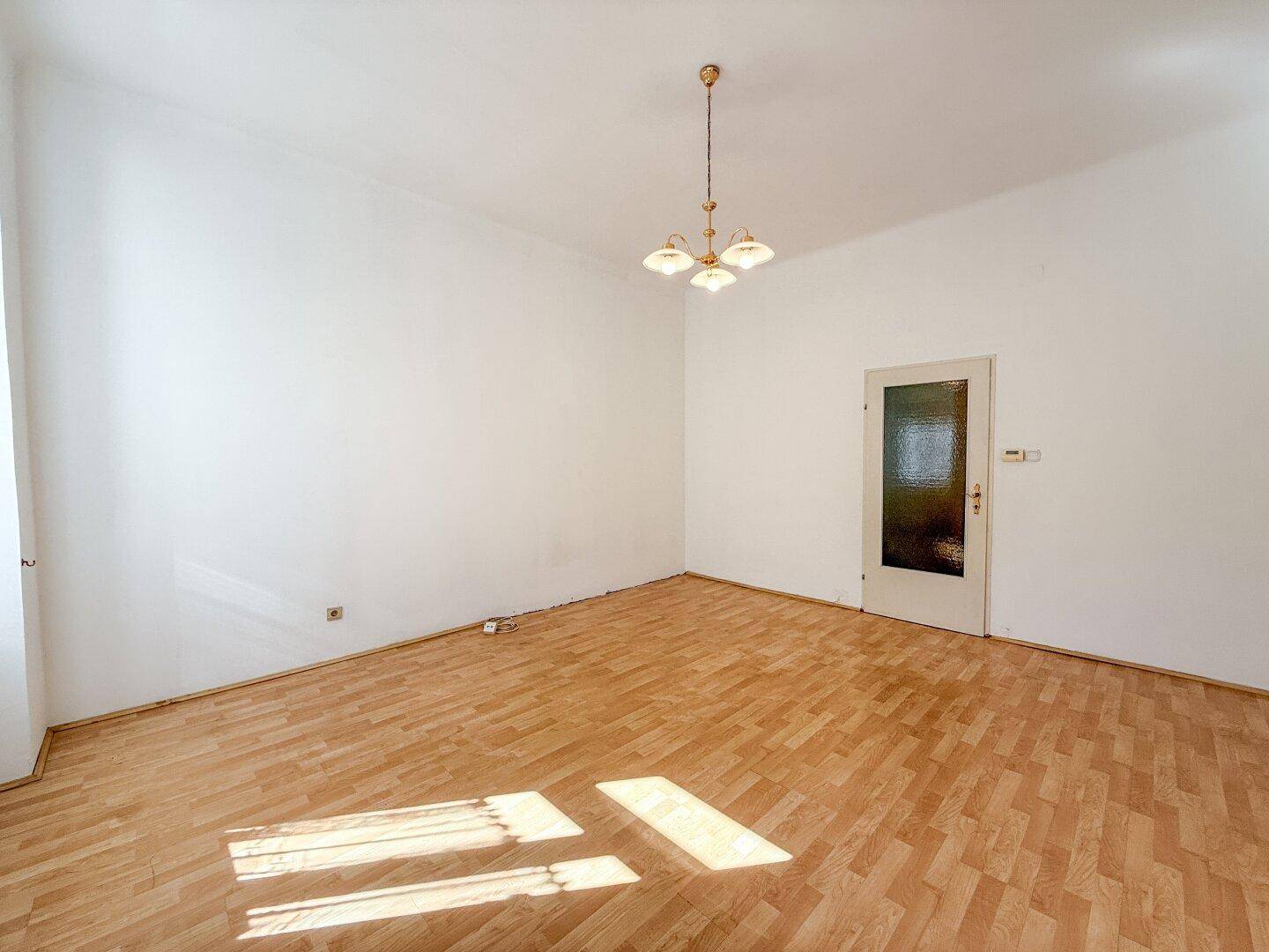 Helles, leeres Zimmer mit Parkettboden und einer Tür, bereit zur individuellen Gestaltung.