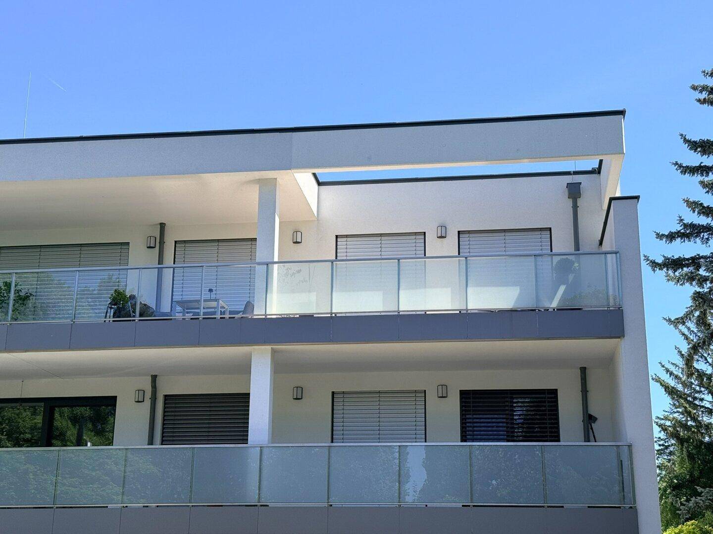 Moderne Architektur mit gestuften Balkonen und Glasgeländern unter strahlend blauem Himmel.