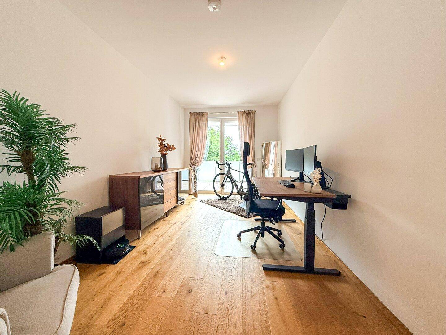 Helles Arbeitszimmer mit Holzboden, modernem Schreibtisch und Blick ins Grüne.