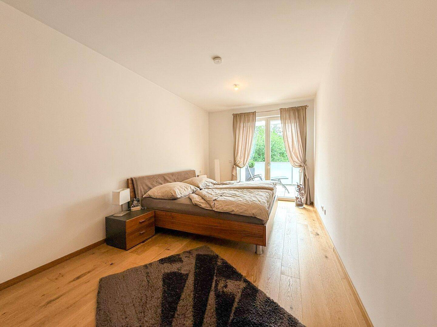 Gemütliches Schlafzimmer mit Holzbett, Parkettboden und Zugang zu einem Balkon.