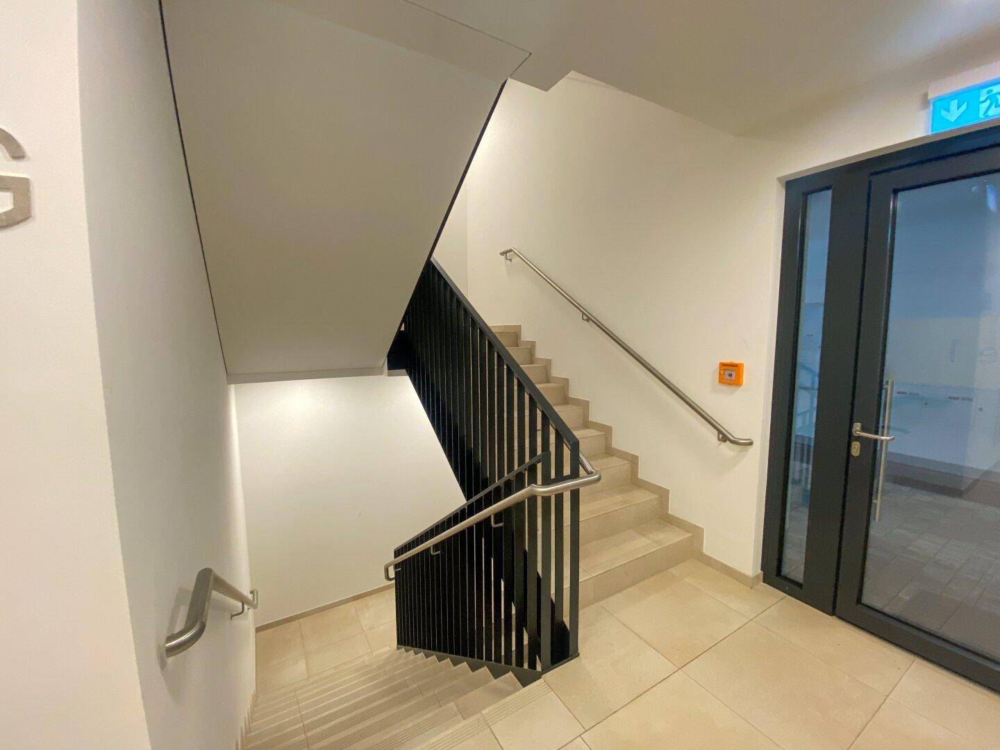 Modernes Treppenhaus mit Metallgeländer und Fliesenboden in einem Mehrfamilienhaus.