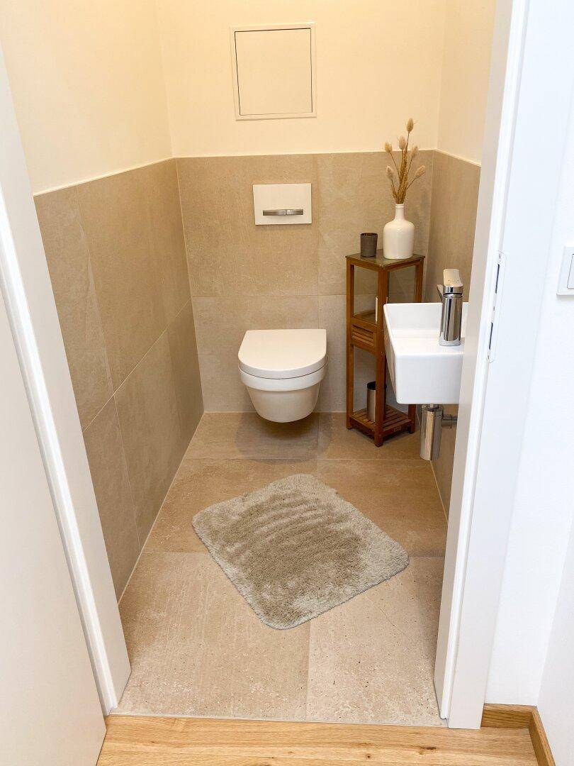 Modernes Gäste-WC mit Wand-WC, kleinem Waschbecken und beigefarbenen Fliesen.