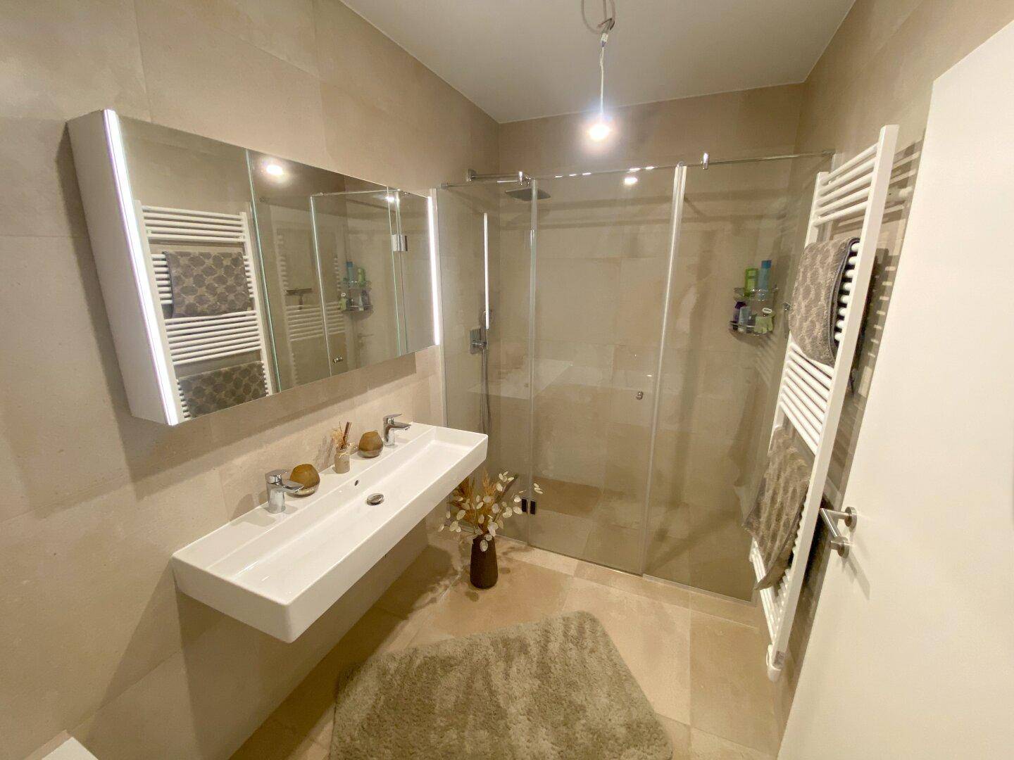 Modernes Badezimmer mit Doppelwaschbecken, großer Dusche und beheiztem Handtuchhalter.
