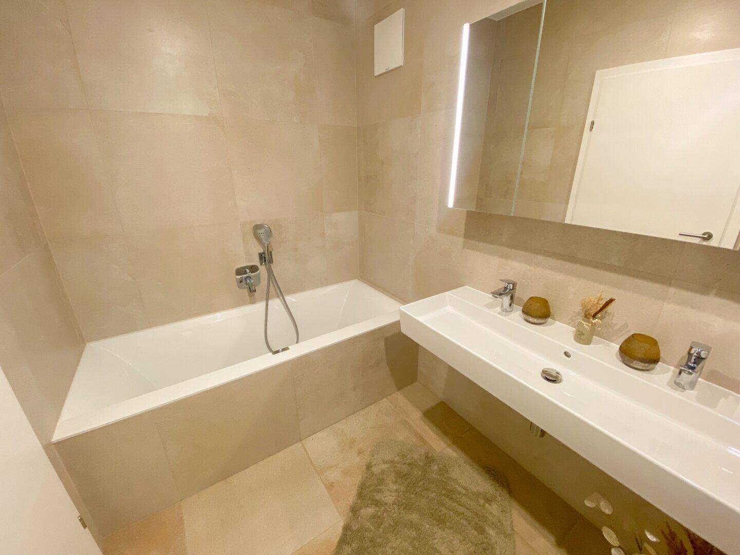 Elegantes Badezimmer mit Badewanne, Doppelwaschbecken und beigefarbenen Wand- und Bodenfliesen.