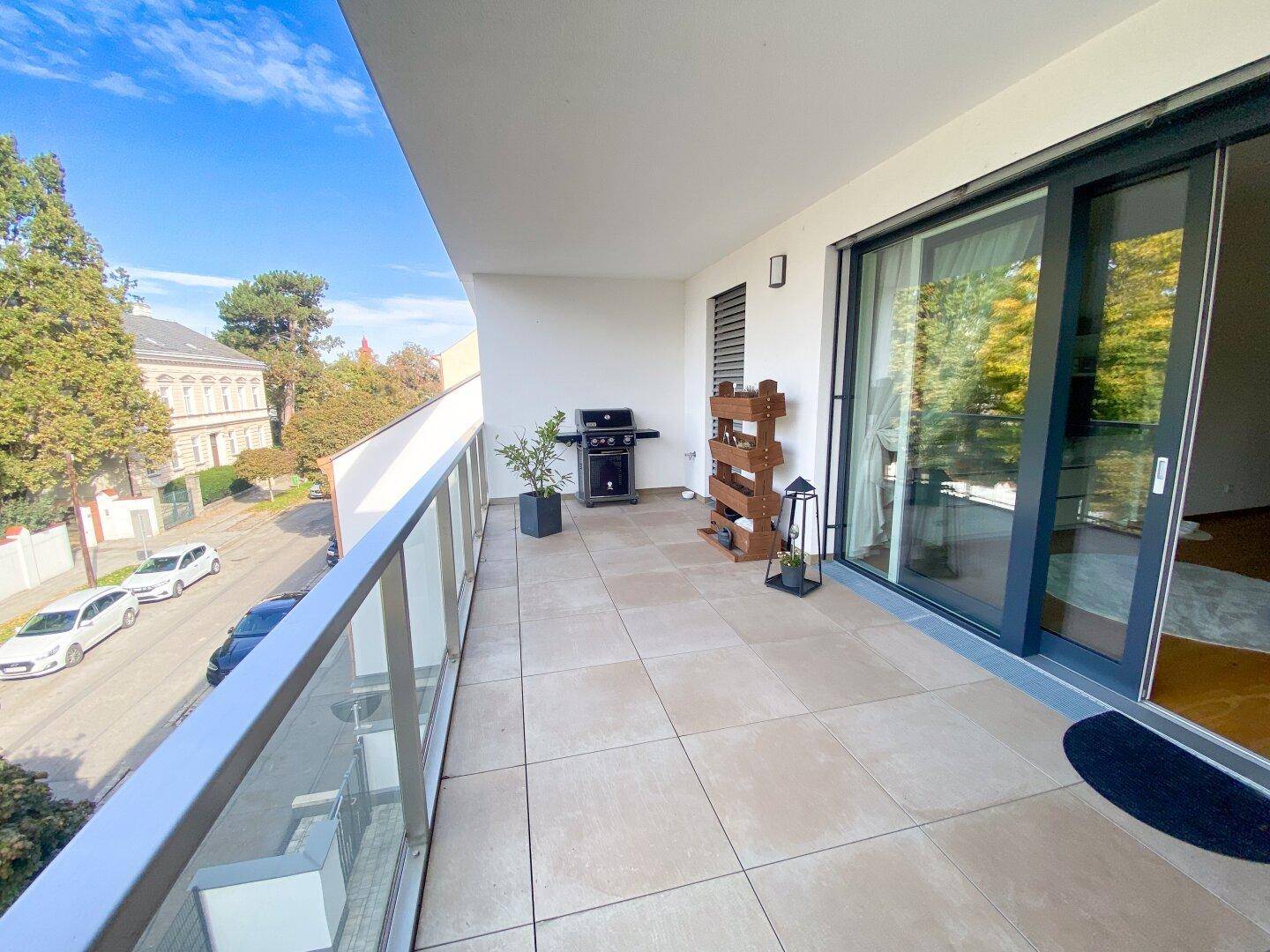 Geräumiger Balkon mit Fliesenboden, Grill und Blick auf die Straße und umliegende Gebäude.