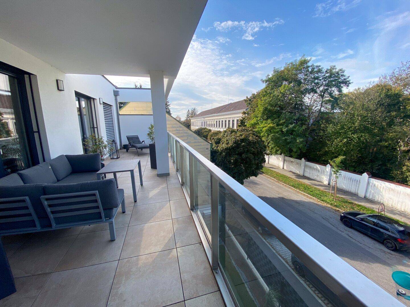 Großer Balkon mit bequemen Gartenmöbeln, Fliesenboden und grüner Aussicht.