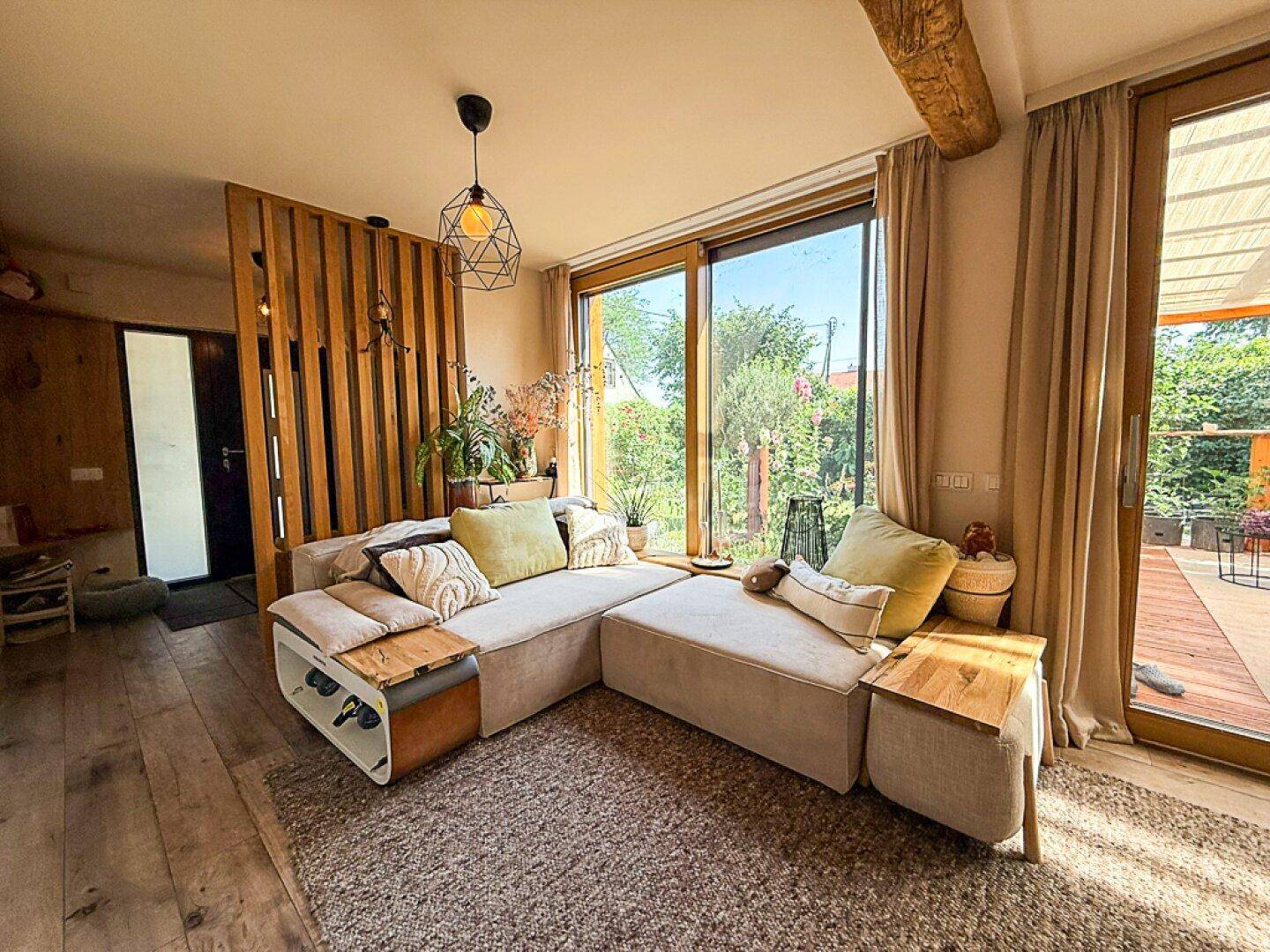 Gemütliches Wohnzimmer mit großem Ecksofa, Holzboden und Zugang zur Terrasse, umgeben von viel Grün.