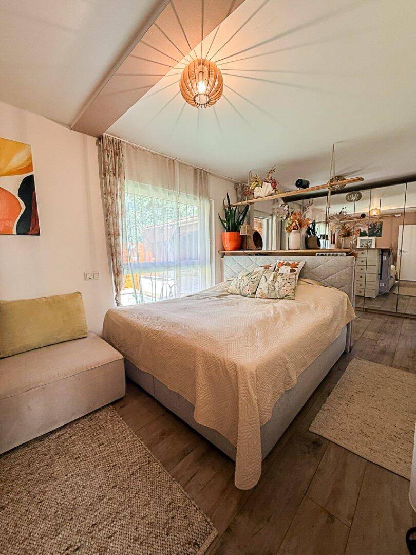 Helles Schlafzimmer mit großem Bett, Holzboden und Spiegelschränken, mit Blick in den Garten.
