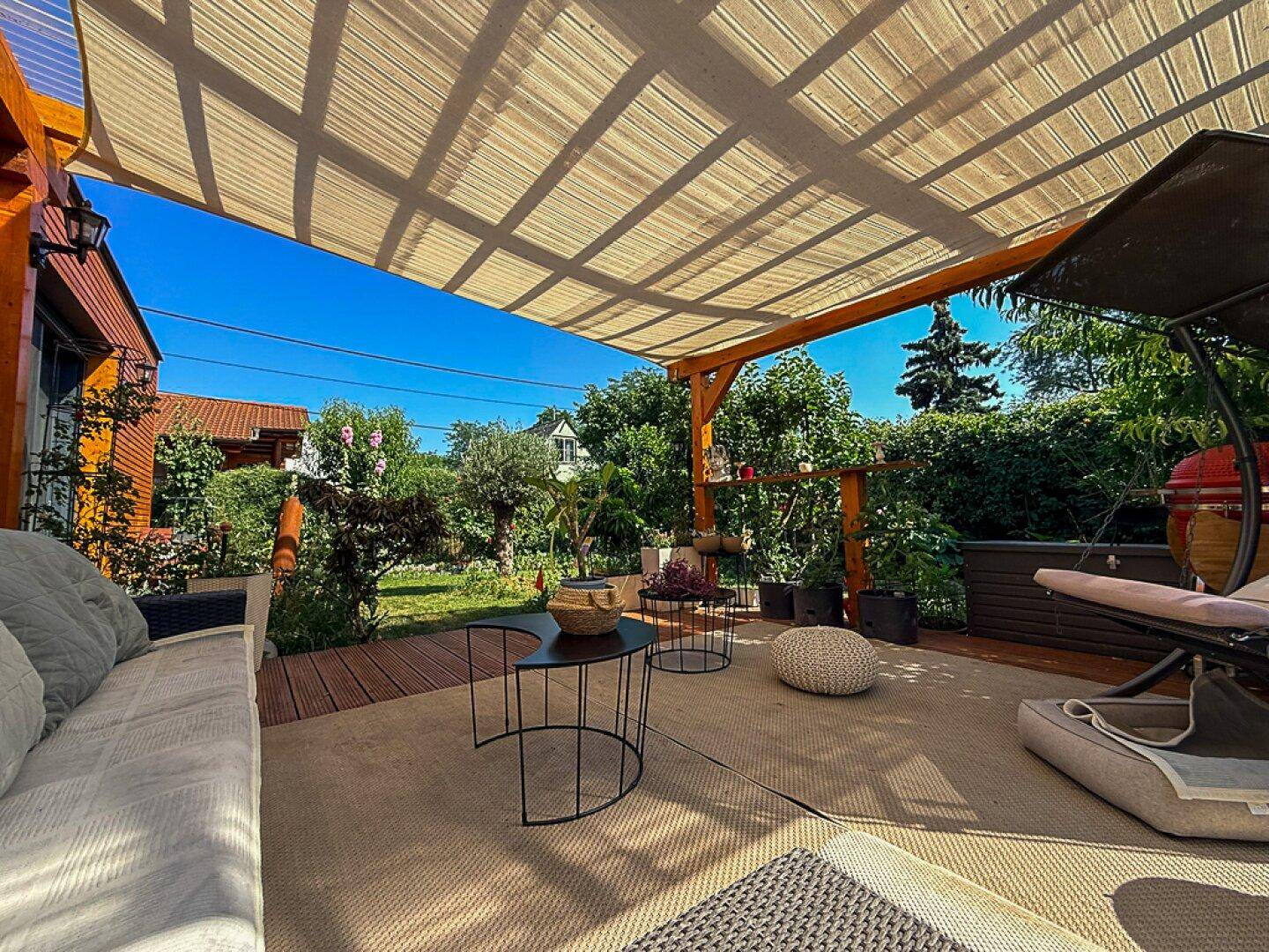 Weitläufige Terrasse mit Pergola und Gartenmöbeln, umgeben von einem gepflegten grünen Garten unter blauem Himmel.