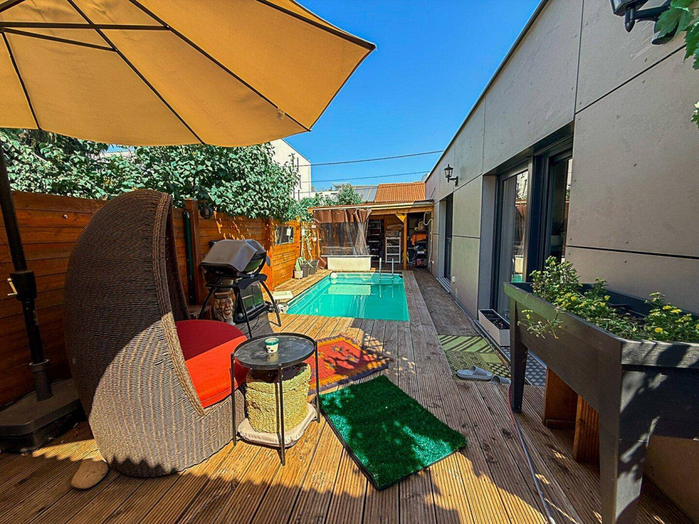 Entspannungsbereich am Pool mit Holzdeck, großem Sonnenschirm und bequemen Outdoor-Möbeln.