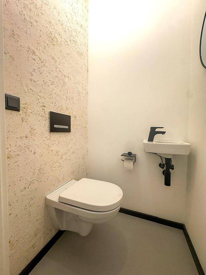Modernes Gäste-WC mit wandhängender Toilette und kleinem Handwaschbecken.