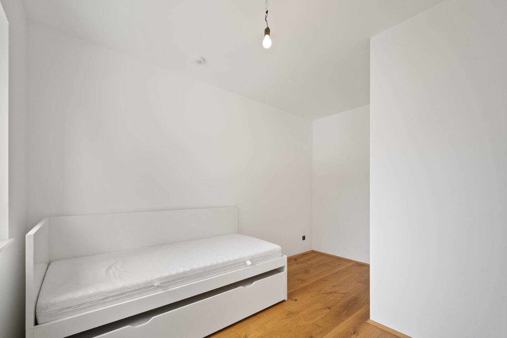 Helles Zimmer mit Holzboden und einem weißen Tagesbett mit Stauraum, ideal als Gästezimmer.