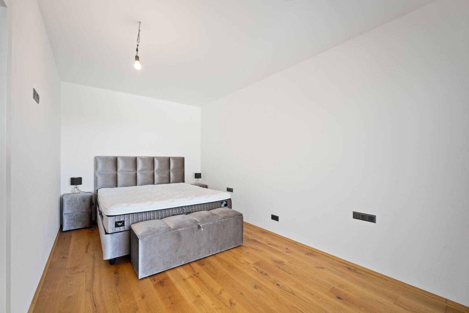 Schlafzimmer mit hellem Holzboden und modernem Polsterbett, bereit zur individuellen Gestaltung.