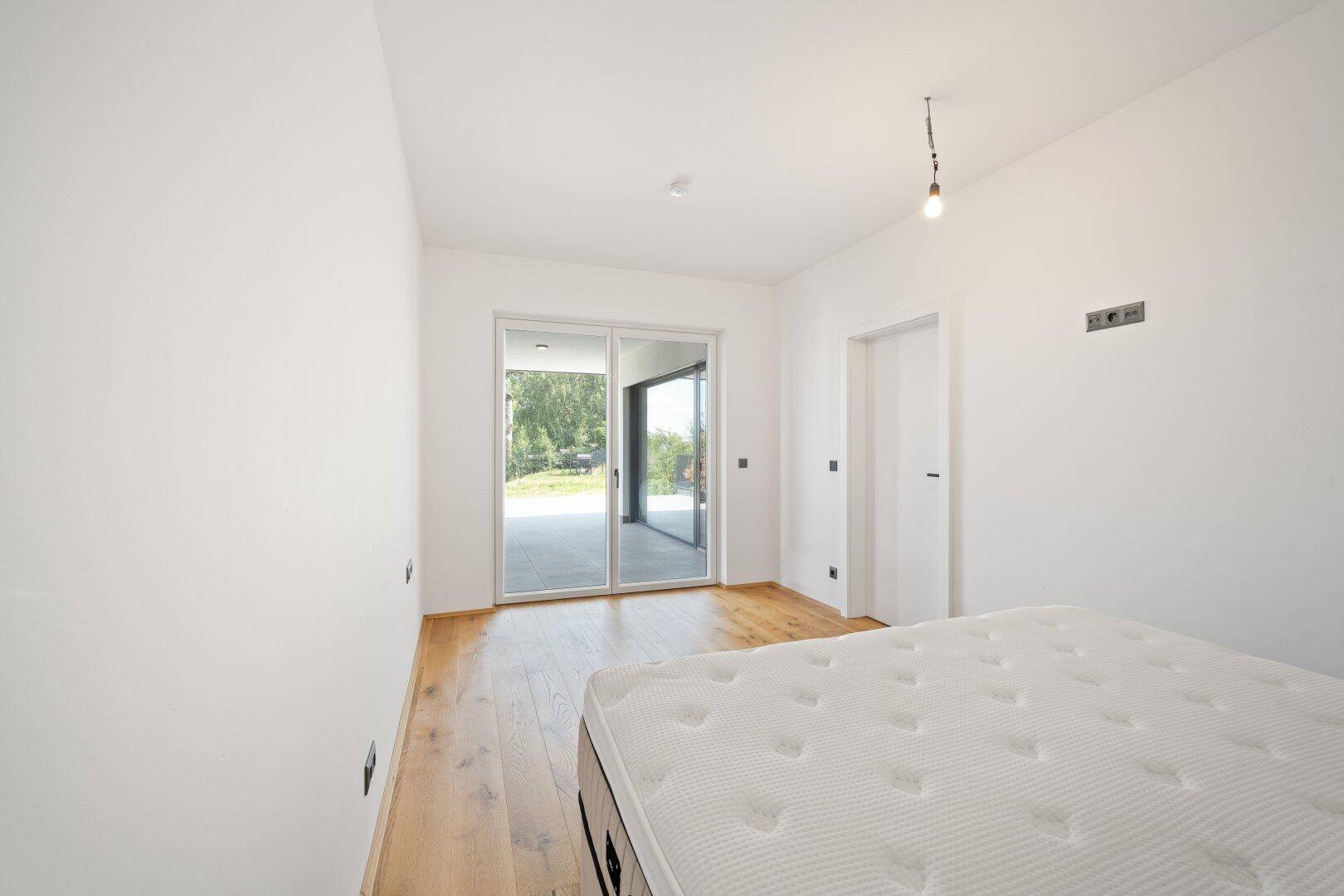 Helles Schlafzimmer mit Zugang zu einer Außenterrasse und Blick ins Grüne.
