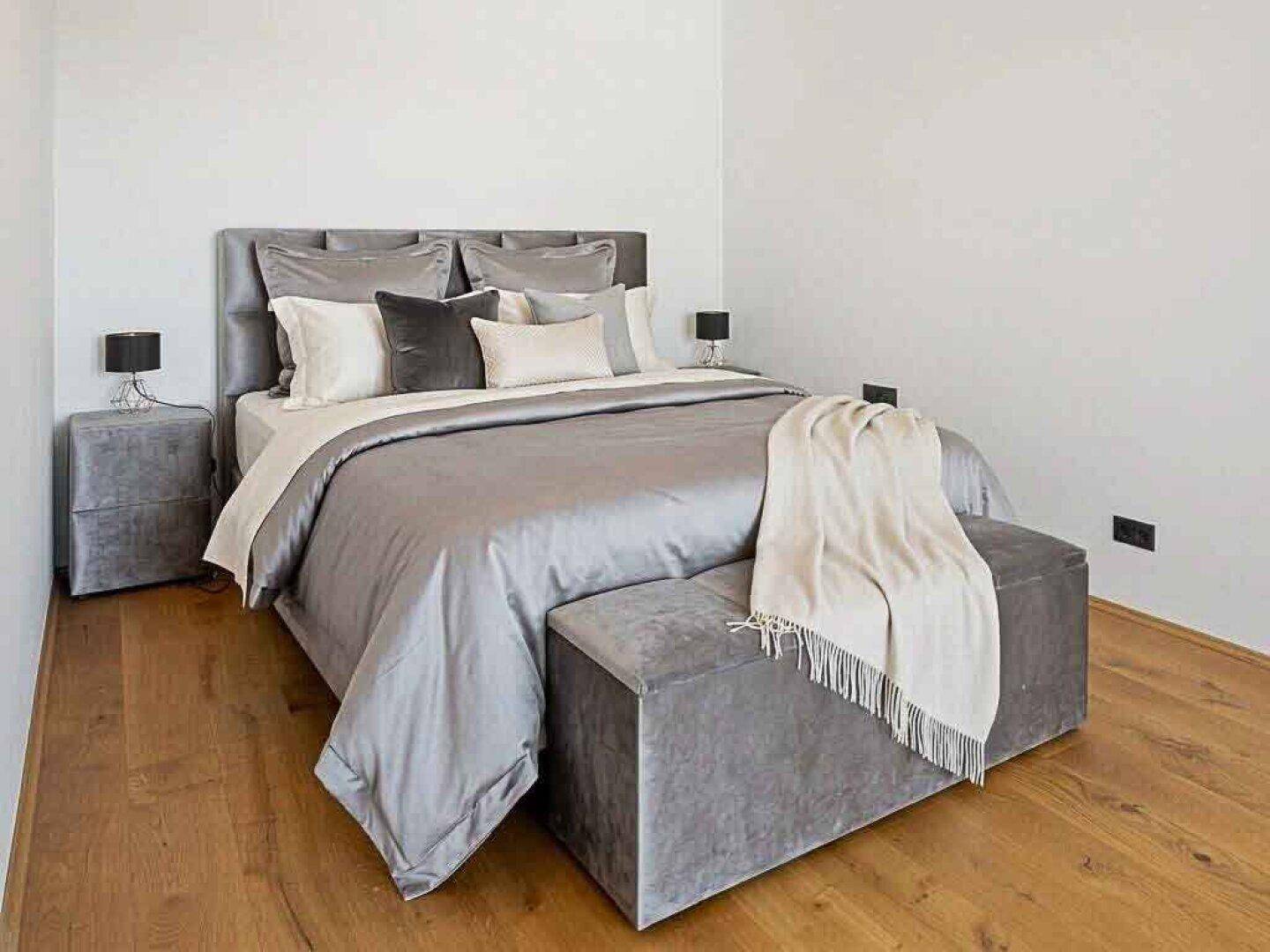 Gemütliches Schlafzimmer mit grauem Polsterbett, passenden Möbeln und warmem Holzboden.