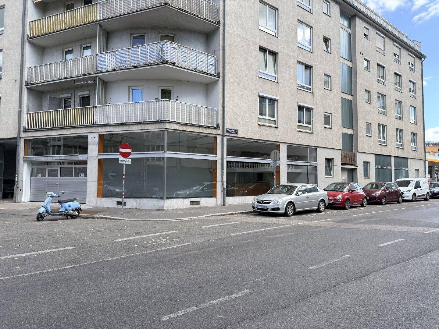 Gesamtansicht des Gebäudes mit Schaufenstern, Balkonen und parkenden Autos auf der Straße.