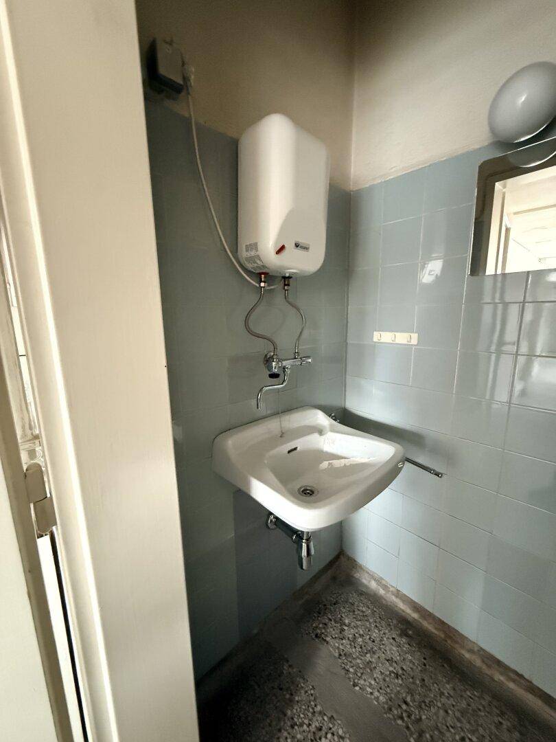 Kleiner Toilettenraum mit Waschbecken, Boiler und hellblauen Fliesen an den Wänden.