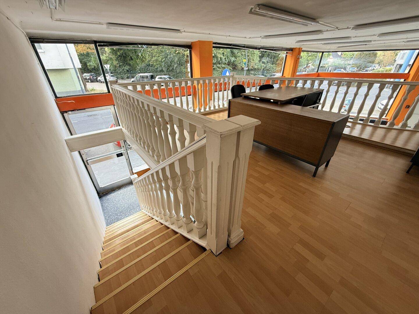 Treppe mit weißem Geländer führt zur Empore mit Holzboden und Bürobereich.