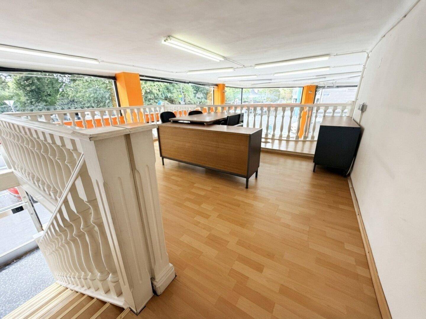 Empore mit Holzboden und Büromöbeln, ideal für einen Arbeitsbereich mit Blick auf den Verkaufsraum.