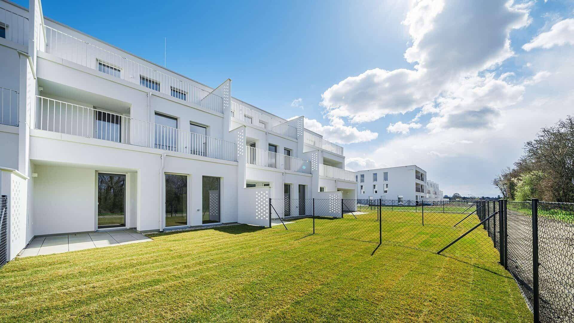 Neubau-Wohngebäude mit gepflegter Rasenfläche und sonnigem Außenbereich unter blauem Himmel.