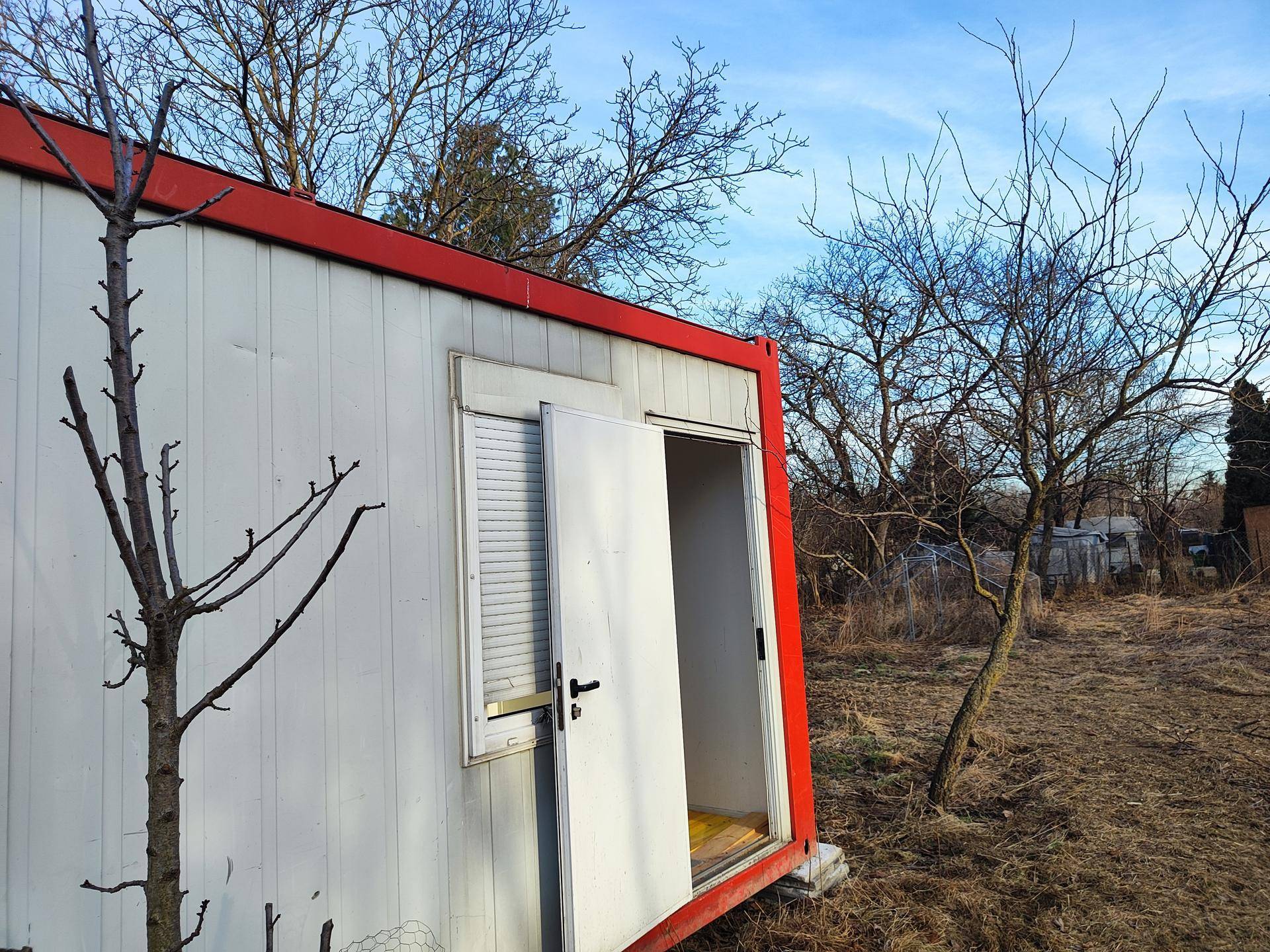 Nahaufnahme eines Containergebäudes mit offener Tür und Fensterladen auf einem ländlichen Grundstück.