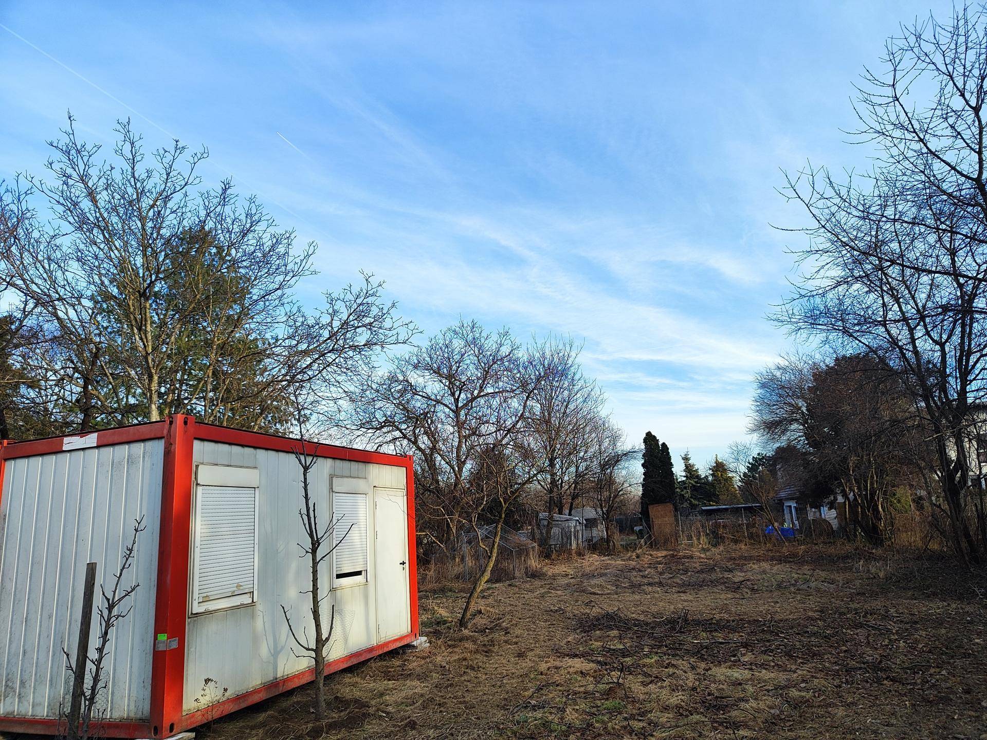 Blick auf ein Containergebäude auf einem Grundstück mit kahlen Bäumen unter blauem Himmel.