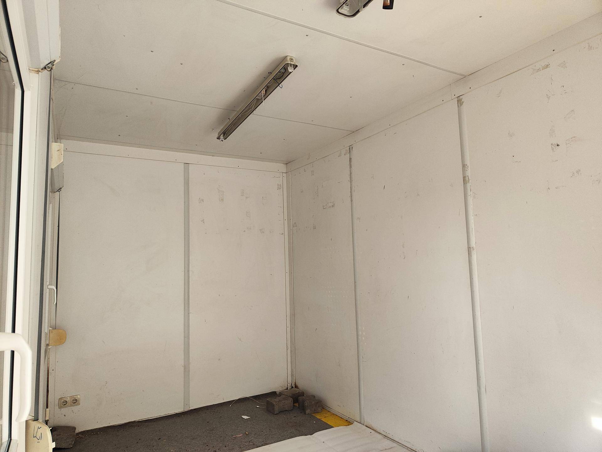 Einfacher Innenraum eines Containergebäudes mit weißen Wänden und Deckenbeleuchtung.