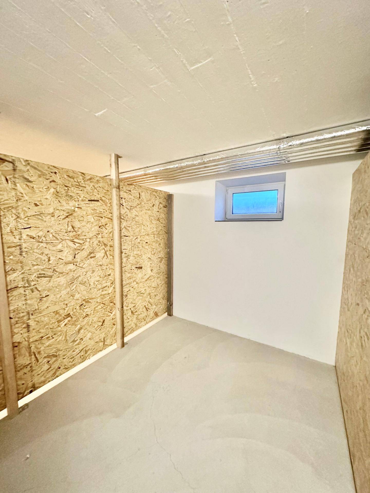 Kellerraum mit Betonboden, kleinem Fenster und einer Wandverkleidung aus OSB-Platten.