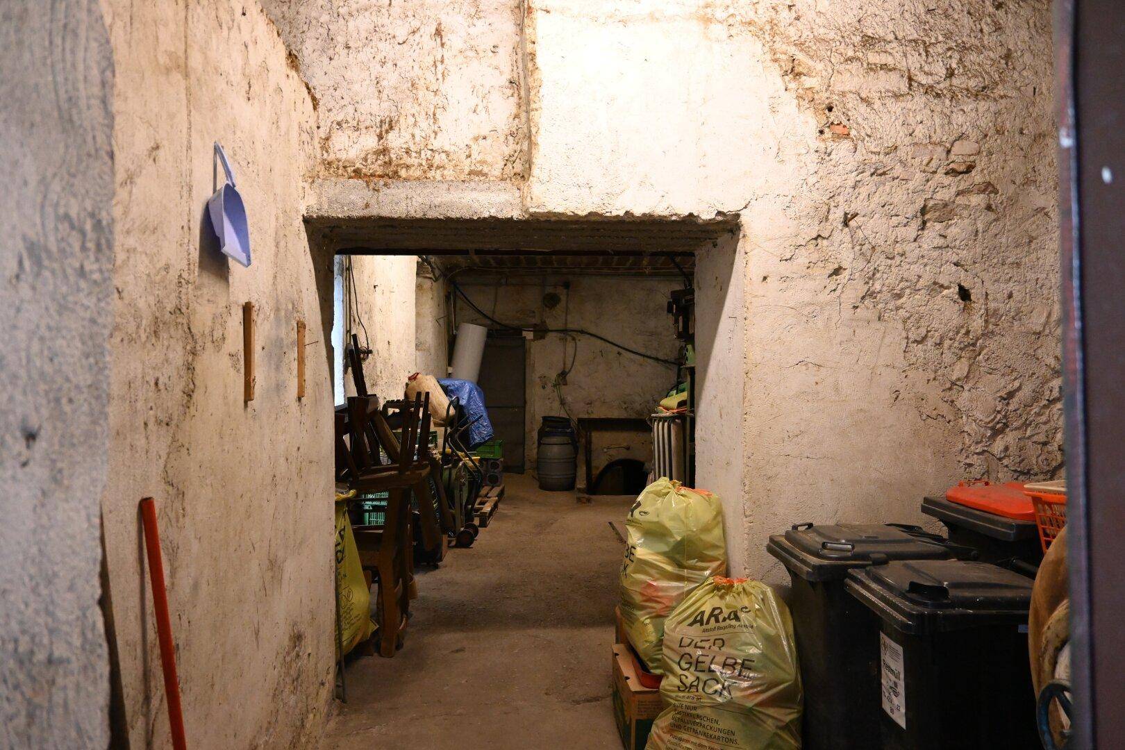 Unfertiger Kellerraum mit rauen Wänden, Betonboden und Lagergegenständen, der sich in Abrisszustand befindet.
