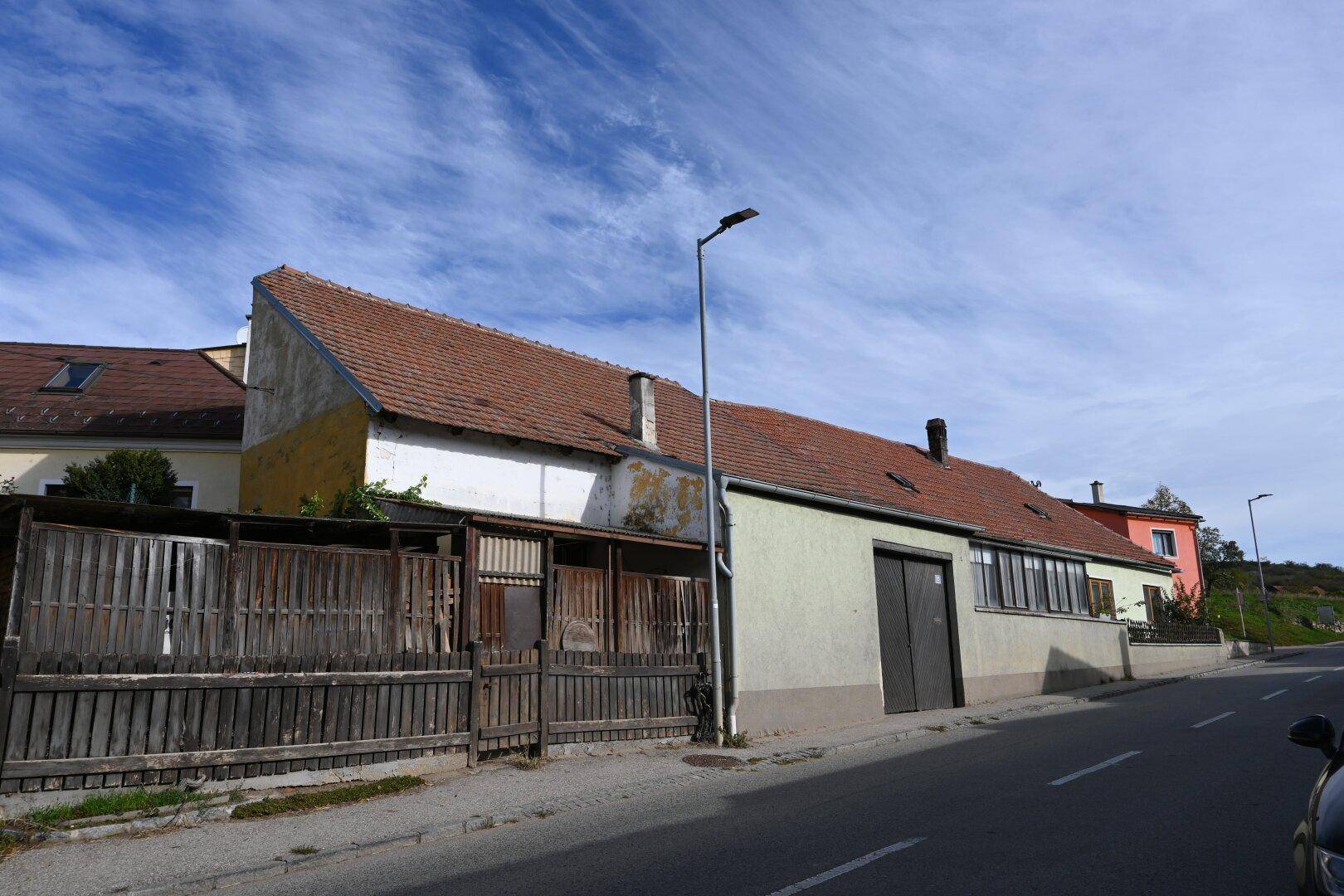 Rückansicht eines älteren Gebäudes mit rotem Ziegeldach und Holzzaun entlang der Straße.