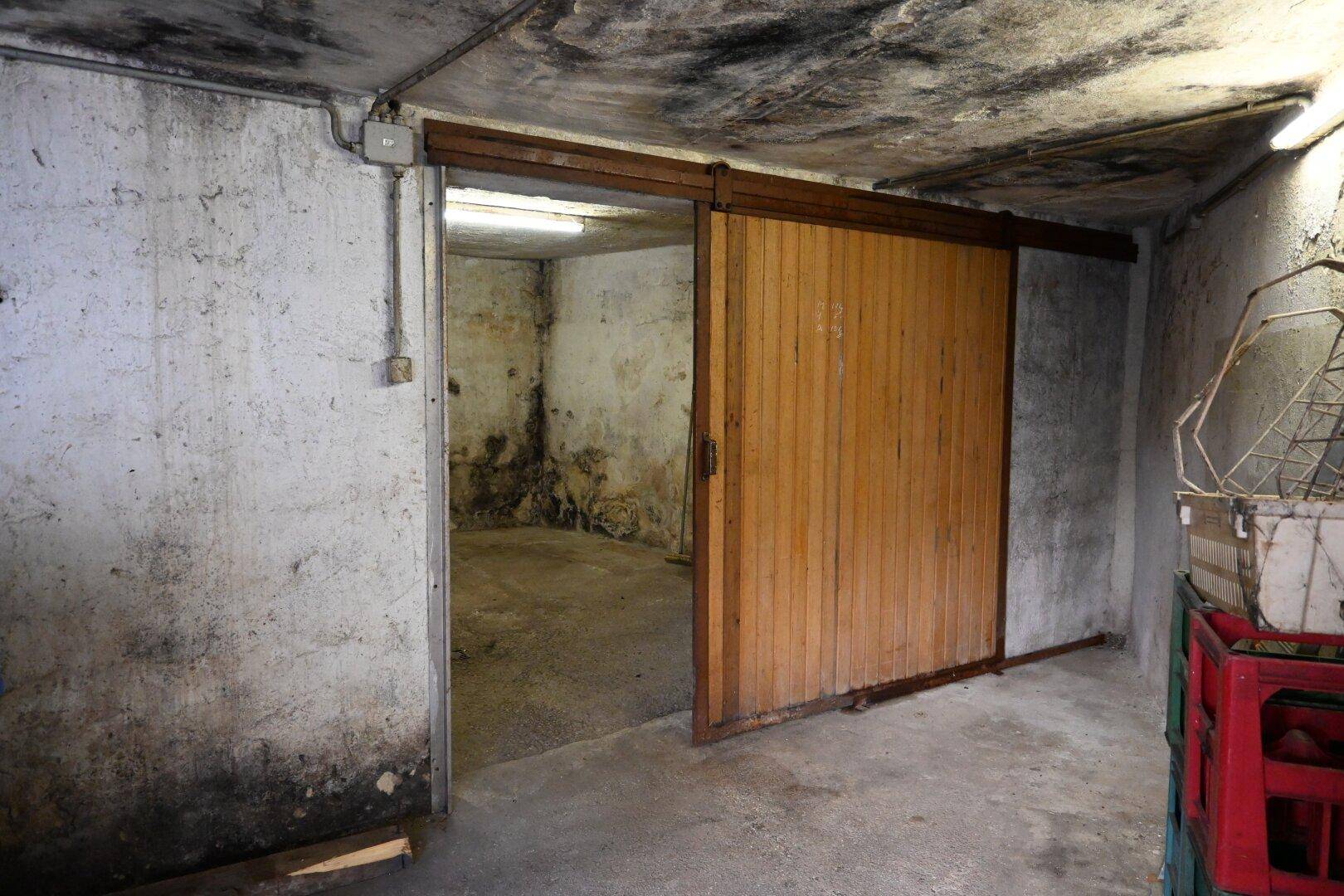 Kellerraum mit Schiebetür aus Holz und sichtbaren Anzeichen von Feuchtigkeit an den Wänden, der sich in Abrisszustand befindet.