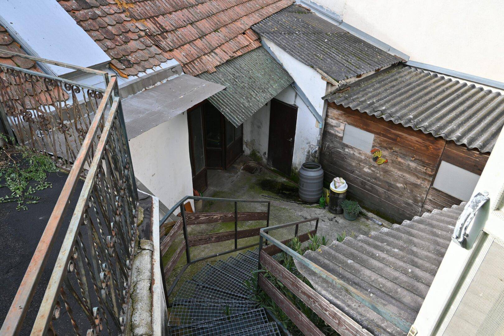 Blick von oben auf den Hinterhof mit Außentreppe, Schuppen und verschiedenen Dächern, die eine Renovierung benötigen.
